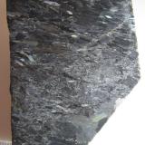 Nuumita (cara pulida)
Nuuk, Kitaa, Groenlandia
6&rsquo;5 x 5 cm.
Nuumita es el nombre común de una roca metasomática formada por los anfíboles antofilita y gedrita.  Los cristales son alargados y dan cierto carácter orientado a la estructura de la roca.  Se observan bonitas irisaciones que hacen la roca muy atractiva, sobre todo en planchas pulidas (de hecho, no es fácil encontrar ejemplares sin pulir). (Autor: prcantos)