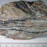 Milonita
Noruega
10 x 4&rsquo;5 cm. (sección transversal) x 9 cm.
Una tectonita bien desarrollada de composición cuarzo-feldespática.  En primer plano se observa la sección transversal (se perciben marcas de corte de la sierra), con su típica estructura debida a la deformación dúctil: las fases minerales de mayor competencia (almendras y nódulos cuarzofeldespáticos) están rodeadas por los minerales menos consistentes que fluyen a su alrededor (filosilicatos oscuros). (Autor: prcantos)