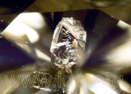 Diamante protogenético incluido en un diamante tallado. Obsérvese las figuras de crecimiento (trígonos) del cristal inclusión. Iluminación de campo oscuro. 40X. (Autor: Egor Gavrilenko)