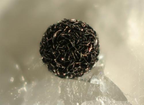 Coarse spherical aggregate of graphite crystals partially dissolved from enclosing calcite matrix, with associated unidentified silicates. (1.2-mm diameter) (Author: John Jaszczak)