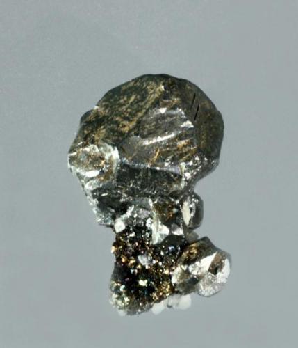 Acantita
Brand-Erbirsdorf, Freiberg, Chemnitz, Sachsen, Alemania. Himmelsfürst (m). (Localidad tipo). 
Cristales cubo-octaédricos (pseudomórficos de argentita), uno de ellos dominante, con la macla de la espinela muy marcada, con pequeños cristales de calcita.
1,8 x 1,2 x 0,9 cm. (Autor: Carles Curto)