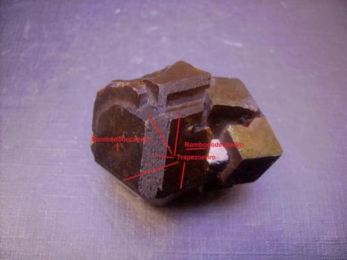 Andradita
Sandaré, Nioro du Sahel Circle, Región de Kayes, Mali
Indicación de las caras sobre el cristal principal. Es lógico que los biseles, las modificaciones, aparezcan generalmente sólo en los cristales mayores. Supongo que un espacio mayor permite la presencia de esas otras caras reducidas. En esta pieza se observan biseles en los cristales mayores, mientras que los más pequeños carecen de ellas. Nuevamente el rombododecaedro modificado por trapezoedro. Otra cuestión para la que no tengo respuesta es por qué a menudo los biseles tienen una textura rugosa como en este caso (recuerdo las fluoritas de La Collada también) mientras que el resto de caras son perfectamente lisas. (Autor: Antonio Alcaide)