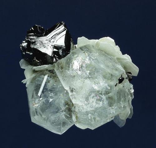 Beryl ( var. Aquamarine ) with Cassiterite
Mt. Xuebaoding, Pingwu County,  Mianyang Prefecture, Sichuan Province, China
63.0 x 52.0 x 32.0 mm overall
Blocky, highly lustrous, pale-blue Aquamarines to 38 mm are topped by a bright black Cassiterite twin measuring 24 x 22 x 20 mm. White Muscovite crystals to 13 mm provide an accent, as do small untwinned Cassiterite crystals to 5 mm. (Author: GneissWare)