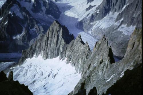 Photo taken from approx. 4,000m on the south arete (ridge) of the Aiguille Verte, looking down at the Aiguille du Moine (3412m) at the end of the arete; where in 1991 I found some crystals!
The stripy glacier is the famous Mer de Glace. 
Photo taken August 1992, by me : )
Scanned from slide photo. (Author: Mike Wood)