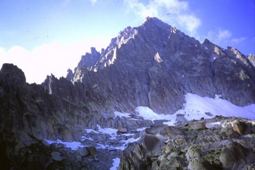 The South Face of the Aiguille du Moine, above the spot where I was bivouacing for the night. The cave where I found the crystals is high on the upper part of the South Face. The next morning I climbed up the mountain from the top of the snowfield, trending leftwards along ledges to reach a gully, which eventually led to the arete on the left. Then the climbing got even harder..
Photo scanned from slide. (Author: Mike Wood)