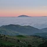 El Djebel Musa asomando sobre un mar de nubes cubriendo el Estrecho sin una brizna de viento, fenómeno poco frecuente por estos lares. Lo normal es lo contrario, con el habitual viento de levante y tiempo despejado, las cumbres de esta y de otras montañas de la zona suelen llevar puesto un sombrero de nubes deshilachadas -las barbas del levante.
La precipitación media anual es de unos 600 mm a nivel del mar y el gradiente pluviométrico de 30 mm/100 m o sea que en la cumbre caen unos 850 mm, buena parte de los cuales (se estima un 45%) se infiltran directamente al acuífero gracias a la escasa vegetación, la estratificación vertical y la fracturación. Al acuífero del conjunto calizo del Djebel Musa, desconectado de otros acuíferos de la sierra colindante al sur por materiales impermeables, se le calculan unos recursos hídricos renovables de 3 Hm3/año. (Autor: Josele)