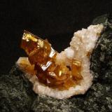 Calcite + chabazite + analcime
Talisker Bay, Isle of Skye, Scotland, UK
Calcite crystals 25 mm

Honey-brown spike of rhombohedral calcite crystals 25mm long stands in a vug (35mm x 20mm) lined with small twinned pinkish chabazite crystals and a single white analcime crystal (3mm). Self-collected 1992 from Talisker Bay, Isle of Skye. (Author: Mike Wood)