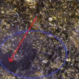 Epidota
Raywoo Mine, Quetta, Balochistán, Pakistán
Detalle de la pieza anterior. Rodeada con un círculo azul la única zona sin el recubrimiento de pequeños cristales amarillos. Se aprecia que tiene buen brillo. También se ven con la lupa y a simple vista con algo de dificultad patrones o lineas paralelas respecto a dos lados (igual en la parte posterior) e inclinadas en esta posición de la pieza (marcada la dirección con la flecha roja). (Autor: Antonio Alcaide)
