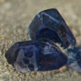 Corundum var sapphire.
Pennycross, W of Loch Scridain, Isle of Mull, Soctland, UK.
Crystal in background is 1 mm across. 37 mm specimen hosts many others, to 4 mm. (Author: Ru Smith)