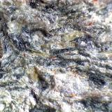 Anfibolita con granate
Río Sucio, Órgiva, Granada, Andalucía, España
60X
Detalle de la roca anterior.  Microfotografía que muestra un granate almandino (izquierda) y los cristales acumulados en su "cola" (sombra de presión), y que son probablemente epidota (verde oliváceo) y anfíbol (verde oscuro o negro), junto a la plagioclasa blanca y la mica clara.  Los minúsculos cristales anaranjados pueden ser zircones, muy abundantes en estas rocas, y que permiten, por sus propiedades radiactivas, efectuar dataciones absolutas. (Autor: prcantos)